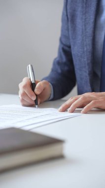 İş adamının zarif bir kalemle kontrat imzalaması, mavi bir takım elbise ve kol saati takması, ofisteki beyaz bir masada oturması. İş adamları konsepti.