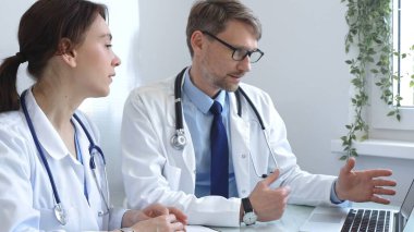 İki doktor bir dizüstü bilgisayardaki tıbbi çizelgeleri dikkatle inceliyor, bir hastane veya klinikte hastanın tıbbi geçmişini tartışıyorlar. Tıp ve sağlık hizmetleri kavramı