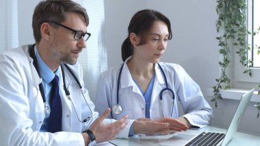 İki doktor bir dizüstü bilgisayarda tıbbi çizelgeleri inceliyor, hastane veya klinik ortamdaki hasta verilerini tartışıyorlar. Tıp ve sağlık hizmetleri kavramı