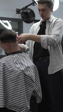 Profesyonel berber müşterilerin saçlarını elektrikli makasla dikkatlice buduyor, modern bir berber dükkanında şık ve kusursuz bir saç kesimi sağlıyor..