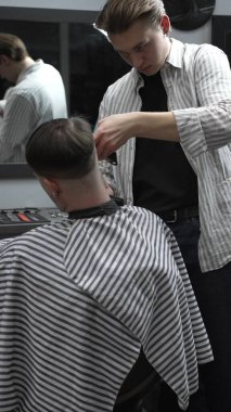 Profesyonel berber müşterilerin saçlarını elektrikli makasla dikkatlice buduyor, modern bir berber dükkanında şık ve kusursuz bir saç kesimi sağlıyor..