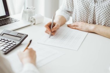 Ofisteki beyaz masada vergileri saymak için dizüstü bilgisayar ve hesap makinesi kullanan iki muhasebeci. İş denetimi ve finans alanında takım çalışması.