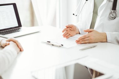 Doktor ve hasta klinikteki beyaz masada oturup bir şeyler tartışıyorlar. Kadın hekim bir kayıt formunu doldururken dinliyor. Tıp konsepti.