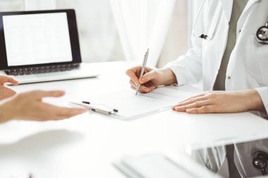 Doktor ve hasta klinikteki beyaz masada oturup bir şeyler tartışıyorlar. Kadın hekim bir kayıt formunu doldururken dinliyor. Tıp konsepti.