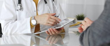 Doktor hastayı muayene ediyor, dijital kayıtlar için tablet tutuyor, modern bir ofis ortamında profesyonel sağlık danışmanlığı sağlıyor. Tıp, sağlık ve bilim konsepti