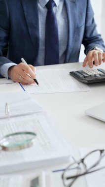 Vergileri hesaplayan ve ofis ortamındaki mali verileri analiz eden profesyonel bir erkek muhasebeci. Ticarette denetim ve vergiler.