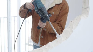Tanımlanamayan inşaat işçisi beton duvarı döner çekiçle yıkıyor, koruyucu güvenlik teçhizatı takıyor, dikey görüntüyü kapatıyor. Yenileme konsepti.