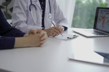 Doktor ve bir hasta klinikteki beyaz masada oturuyorlar. Kadın hekim muayene sırasında not almak için pano kullanıyor. Kapatın. Tıp konsepti.