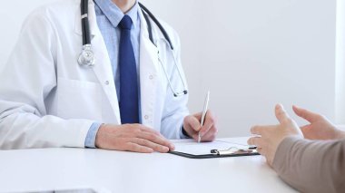 Yetişkin bir doktor, klinikteki bir muayenede kadın bir hastanın semptomlarını açıklarken not alıyor. İlaç ve sağlık hizmetleri kavramı.