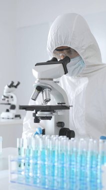 Koruyucu ekipman alanında çalışan bir tıp virologu laboratuvar ortamında araştırma yaparken mikroskop altında virüs örneklerini inceliyor..