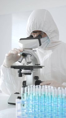 Koruyucu ekipman alanında çalışan bir tıp virologu laboratuvar ortamında araştırma yaparken mikroskop altında virüs örneklerini inceliyor..