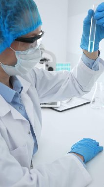 Mavi kapaklı, eldivenli ve Google 'lı tıp bilimi araştırmacısı laboratuvar çalışma alanında test tüpündeki sıvıyı inceliyor. İlaç ve sağlık hizmetleri kavramı.