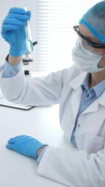 Mavi kapaklı, eldivenli ve Google 'lı tıp bilimi araştırmacısı laboratuvar çalışma alanında test tüpündeki sıvıyı inceliyor. İlaç ve sağlık hizmetleri kavramı.