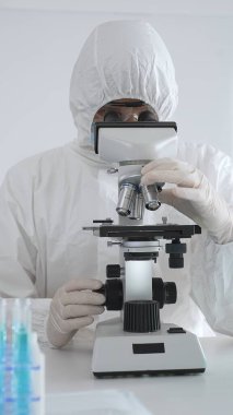 Koruyucu ekipman alanında çalışan bir tıp virologu laboratuvar ortamında araştırma yaparken mikroskop altında virüs örneklerini inceliyor..