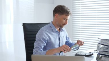 Muhasebeci, mali belgeleri büyüteçle dikkatlice inceleyerek ofisinin çalışma alanındaki detaylara hassasiyet ve dikkat sağlamış. İş dünyasında denetim ve vergi teması