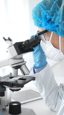 Erkek kıdemli bilim araştırmacısı örnek incelerken hassas mikroskobu kalibre ederek steril laboratuvar ortamındaki çığır açan tıbbi araştırmaları araştırıyor. Tıp ve bilim konsepti.