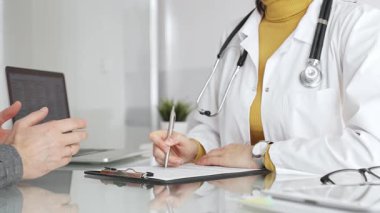 Doktor tıbbi bir randevu sırasında panoya notlar yazıyor, modern bir hastane ofisinde bir hastayla sağlık hakkında konuşuyor. Tıp, sağlık ve bilim konsepti