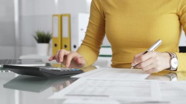 Kişisel mali işlerle ilgilenen, masrafları ve geliri hesaplayan, faturaları inceleyen ve masa başında vergi formları hazırlayan bir kadın. İş dünyasında denetim ve vergi teması