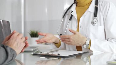 Doktor tıbbi bir randevu sırasında panoya notlar yazıyor, modern bir hastane ofisinde bir hastayla sağlık hakkında konuşuyor. Tıp, sağlık ve bilim konsepti