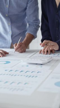 İş arkadaşları birlikte çalışıyor, finansal tabloları analiz ediyor ve bir ofis toplantısında şirket performansını tartışmak ve gelecekteki stratejileri planlamak için hesap makinesi kullanıyorlar..