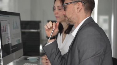 Proje detaylarını tartışan ve bilgisayar ekranında mali verileri analiz eden profesyonel meslektaşlar, modern ofis ortamında takım çalışmasını ve işbirliğini teşvik ediyor