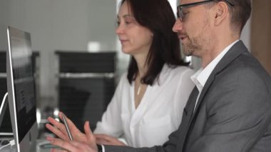 Proje detaylarını tartışan ve bilgisayar ekranında mali verileri analiz eden profesyonel meslektaşlar, modern ofis ortamında takım çalışmasını ve işbirliğini teşvik ediyor