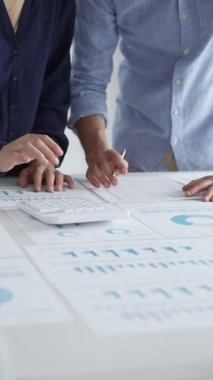 İş arkadaşları birlikte çalışıyor, finansal tabloları analiz ediyor ve bir ofis toplantısında şirket performansını tartışmak ve gelecekteki stratejileri planlamak için hesap makinesi kullanıyorlar..