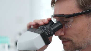 Güvenlik gözlüğü takan ve modern bir laboratuvarda mikroskop kullanan olgun bir bilim adamının araştırma ve analize odaklandığı bir fotoğrafı. Tıp, sağlık ve bilim konsepti