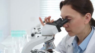 Kadın bilim adamı mikroskop örneklerini analiz ediyor, çağdaş laboratuvar ortamında gelişmiş ekipmanlarla tıbbi tedavileri araştırıyor. Tıp, sağlık ve bilim konsepti