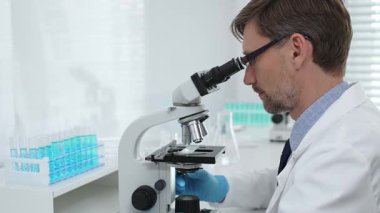 Gelişmiş laboratuvar araştırmaları sırasında mikroskopla biyolojik örnekleri inceleyen odaklanmış bir tıp bilimcisi. Tıp, sağlık ve bilim konsepti