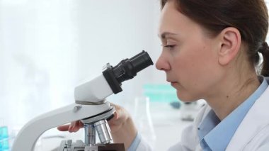 Kadın bilim adamı mikroskop örneklerini analiz ediyor, çağdaş laboratuvar ortamında gelişmiş ekipmanlarla tıbbi tedavileri araştırıyor. Tıp, sağlık ve bilim konsepti