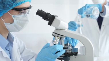 Koruyucu giysili kadın bilim adamı mikroskop altında numuneleri incelerken laboratuvar asistanı profesyonel bir tıbbi araştırmada cam ile ilgileniyor. Tıp ve bilim konsepti.