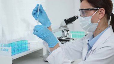 Laboratuvar analizi sırasında cam şişeye kimyasal solüsyon yerleştiren koruyucu giysi araştırmacısı, beyaz arka plan. Tıp, sağlık ve bilim konsepti