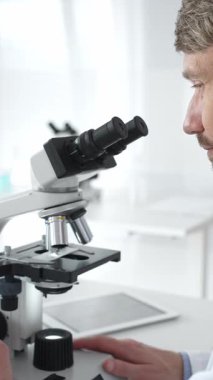 Parlak bir laboratuvarda mikroskopla gözlem yapan bir bilim adamı yeni ilaçlar ve tedaviler geliştirmek için araştırma yapıyor. Tıp ve bilim konsepti.