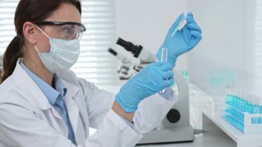 Laboratuvar analizi sırasında cam şişeye kimyasal solüsyon yerleştiren koruyucu giysi araştırmacısı, beyaz arka plan. Tıp, sağlık ve bilim konsepti