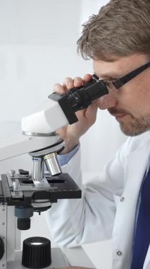 Gözlük takan erkek bilim adamı mikroskop altında araştırma ve analiz yaparak bilimsel araştırmaları ve keşifleri gösteriyor. Tıp ve bilim konsepti.