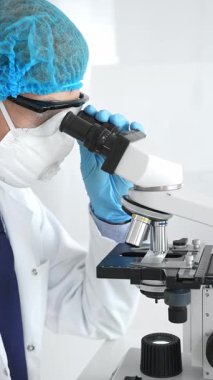 Erkek kıdemli bilim araştırmacısı örnek incelerken hassas mikroskobu kalibre ederek steril laboratuvar ortamındaki çığır açan tıbbi araştırmaları araştırıyor. Tıp ve bilim konsepti.
