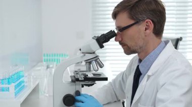 Gelişmiş laboratuvar araştırmaları sırasında mikroskopla biyolojik örnekleri inceleyen odaklanmış bir tıp bilimcisi. Tıp, sağlık ve bilim konsepti