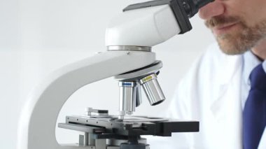 Yetişkin bir bilim adamını dikkatlice mikroskop kullanarak, laboratuvar ortamında örnek inceleyerek, önemli araştırmalar yaparak yakınlaştır. Tıp ve bilim konsepti.