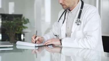 Steteskoplu beyaz önlüklü bir doktor klinikte tıbbi bakım ve profesyonel hizmetler sağlayan bir belge hazırlıyor. Tıp, sağlık ve bilim konsepti