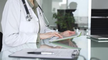 Ofis masasında steteskop kullanan beyaz önlüklü doktor, tele sağlık ve klinik bakım yenilikleri için dijital hasta verilerini inceliyor. İlaç ve sağlık hizmetleri kavramı