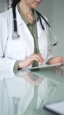 Ofis masasında steteskop kullanan beyaz önlüklü doktor, tele sağlık ve klinik bakım yenilikleri için dijital hasta verilerini inceliyor. İlaç ve sağlık hizmetleri kavramı