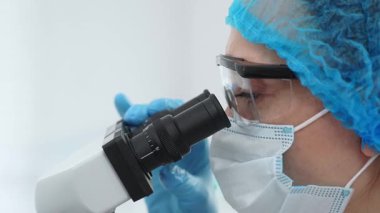 Mikroskop kullanan, maske, gözlük ve eldiven takan bir bilim adamının laboratuvar ortamında araştırma yapmasını. Tıp, sağlık ve bilim konsepti