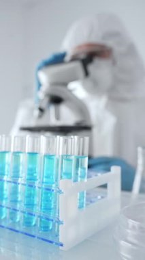 Koruyucu ekipman ve mavi eldiven giyen bilim araştırmacısı veya virolog tıbbi laboratuvar araştırması sırasında mikroskop lenslerini ayarlıyor. Tıp, sağlık ve bilim konsepti.