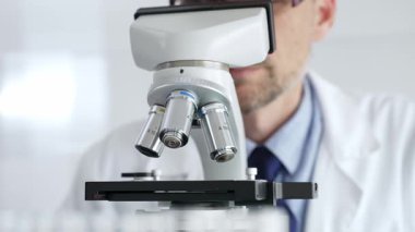 Beyaz önlüklü ve mavi eldivenli, mikroskop ayarlayan, modern laboratuarda ilaç araştırması yapan erkek bilim adamlarına yaklaş. Tıp ve bilim konsepti.