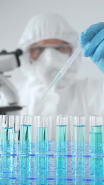 Koruyucu ekipman takan bilim araştırmacısı, tıbbi araştırma deneyi yaparken deney tüplerine sıvıyı dikkatlice yerleştiriyor. Tıp, sağlık ve bilim konsepti.