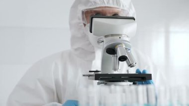 Koruyucu ekipman takan bilim araştırmacısı mikroskobu ayarlıyor, laboratuvar örneklerini steril araştırma ortamında hassasiyetle analiz ediyor. Tıp, sağlık ve bilim konsepti.