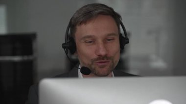 Erkek müşteri hizmetleri temsilcisi, modern bir çalışma alanında sanal iletişim araçları kullanılarak çevrimiçi destek sunarak müşterilerle iletişim ve yardım sağlıyor. İş konsepti.