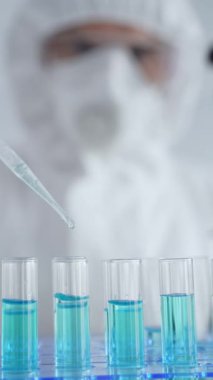 Koruyucu ekipman takan bilim araştırmacısı, tıbbi araştırma deneyi yaparken deney tüplerine sıvıyı dikkatlice yerleştiriyor. Tıp, sağlık ve bilim konsepti.