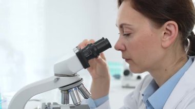 Kadın bilim adamı mikroskop örneklerini analiz ediyor, çağdaş laboratuvar ortamında gelişmiş ekipmanlarla tıbbi tedavileri araştırıyor. Tıp, sağlık ve bilim konsepti